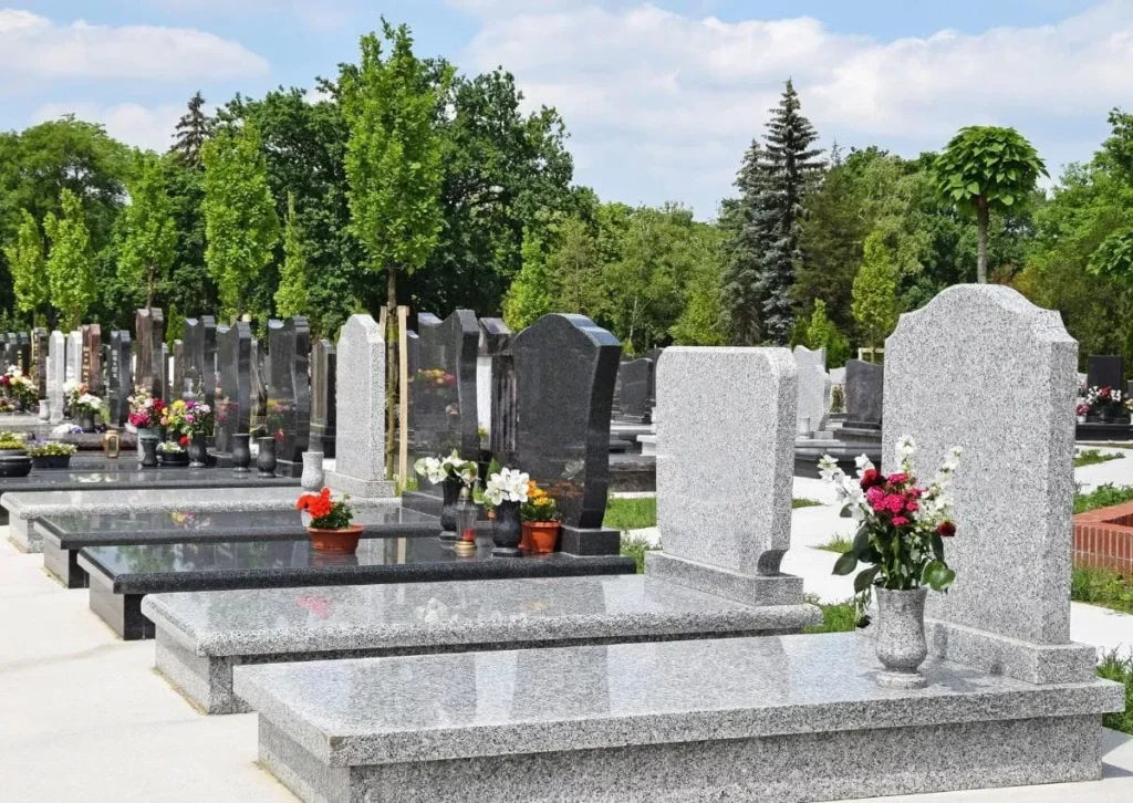 Monuments funéraires en granit gris et noir alignés dans un cimetière paysagé.